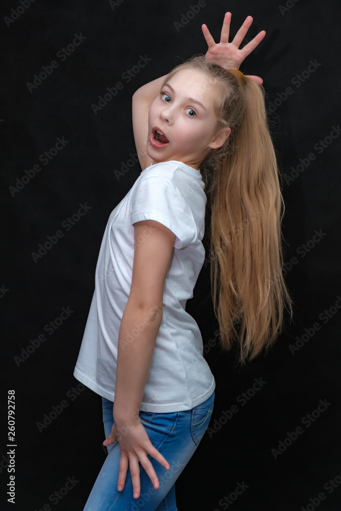 Concept portrait of a cute pretty blonde teen girl with long hair posing in white t-shirt on black background in studio.