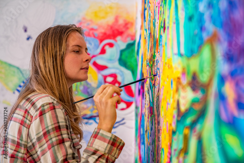 Joyful young female artist painting on the wall, using brush and bright acrylic paints photo