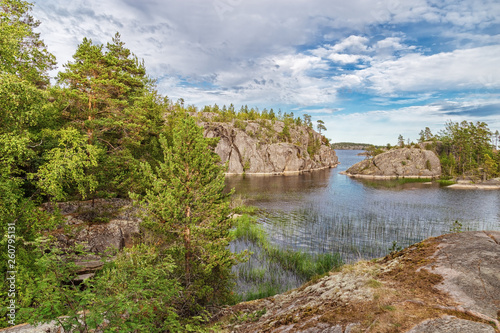 Beautiful view of Lake Ladoga and small stone Islands covered trees and grass. Blue sky with clouds. Republic Of Karelia, Russia.