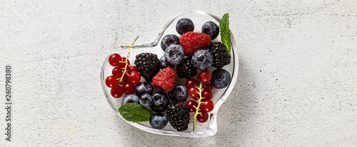 Fresh ripe berries in a glass heart-shaped bowl on a stone white table. summer season. healthy recipes and drinksrries in a glass heart-shaped bowl on a stone white table. summer season. 