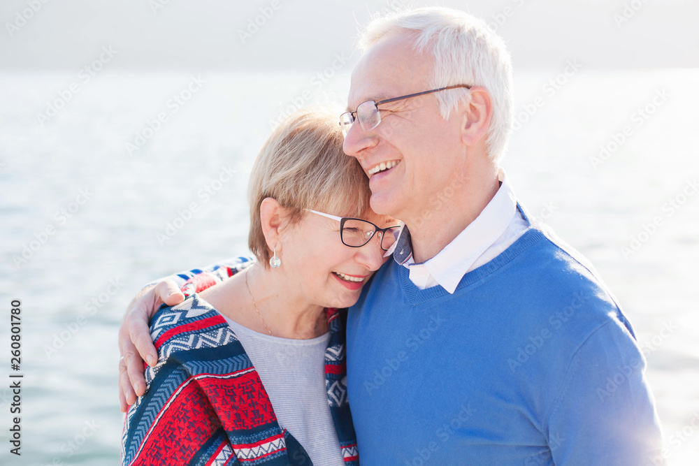 Senior couple is laughing, smiling at sea beach outdoor. Happy man and woman are hugging, embracing, enjoying retirement. Concept of wellbeing, happiness, male and female health, lifestyle moments. Senior couple is laughing, smiling at sea beach outdoor. Happy man and woman are hugging, embracing, enjoying retirement. Concept of wellbeing, happiness, male and female health, lifestyle moments.