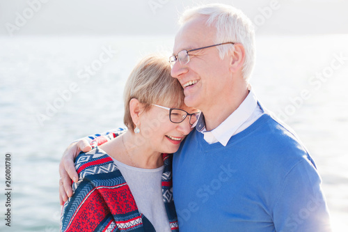 Senior couple is laughing, smiling at sea beach outdoor. Happy man and woman are hugging, embracing, enjoying retirement. Concept of wellbeing, happiness, male and female health, lifestyle moments. © Marina April