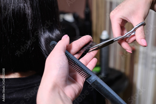 Hairdresser makes a hairstyle brunette girl in a beauty salon with scissors and comb .