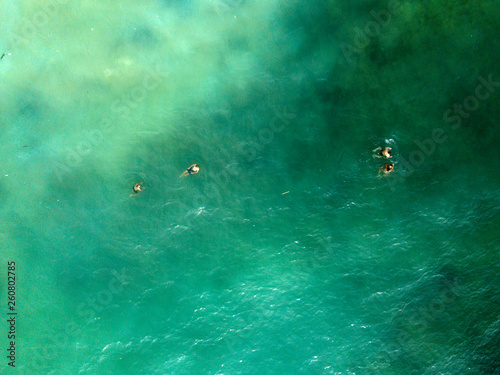 Aerial view of people swimming on waves in sea, ocean on Dreamland beach, Bali, Indonesia.