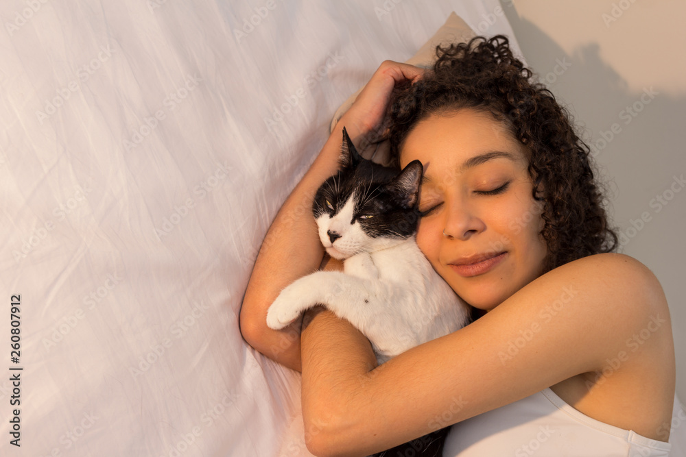 Portrait of woman with curly hair sleeping with her black and white cat in bed. Concept of love to animals, pets, care, tranquility, peace. Portrait of woman with curly hair sleeping with her black and white cat in bed. Concept of love to animals, pets, care, tranquility, peace.