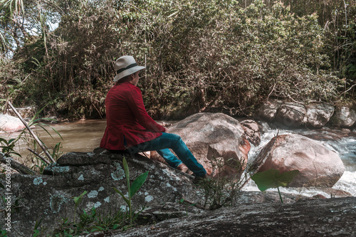 adult man sitting on a rock by the river resting quietly in a very quiet scene