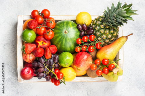 Fototapeta Naklejka Na Ścianę i Meble -  Healthy raw rainbow fruits, mango papaya strawberries limes watermelon pineapple tomatoes in white box on light concrete background, top view, selective focus