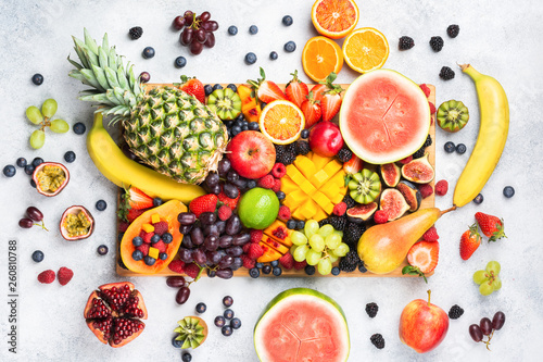 Healthy raw rainbow fruit platter background  mango papaya strawberries oranges blueberries pineapple watermelon on wooden board on light concrete background  top view  selective focus