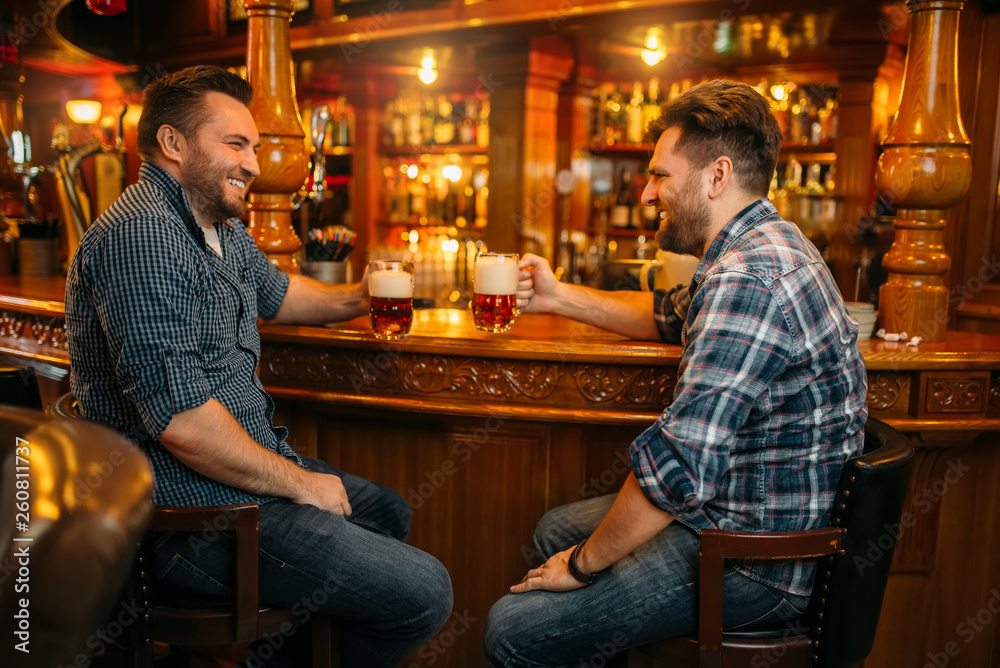 Two male friends drinks beer at the counter in pub