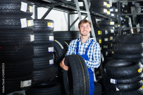 young happy mechanic man working with car tires in workshop