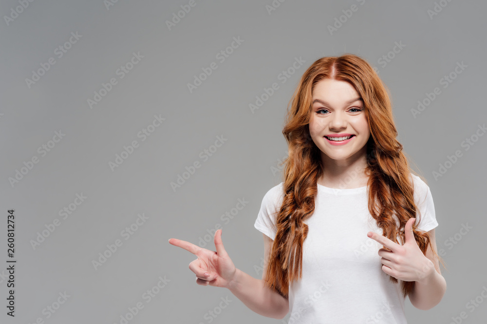 beautiful redhead girl looking at camera, smiling and pointing with fingers isolated on grey with copy space beautiful redhead girl looking at camera, smiling and pointing with fingers isolated on grey with copy space