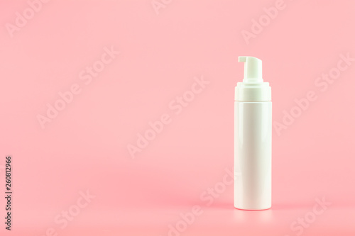 White plastic cosmetic lotion bottle on pink background.