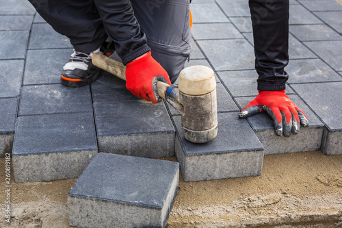 Hands of worker installing concrete paver blocks with rubber hammer photo