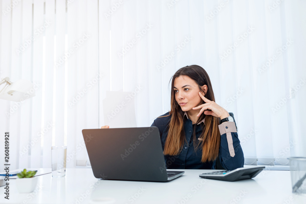 Beautiful young business woman sitting behing her desk in an office. Beautiful young business woman sitting behing her desk in an office.
