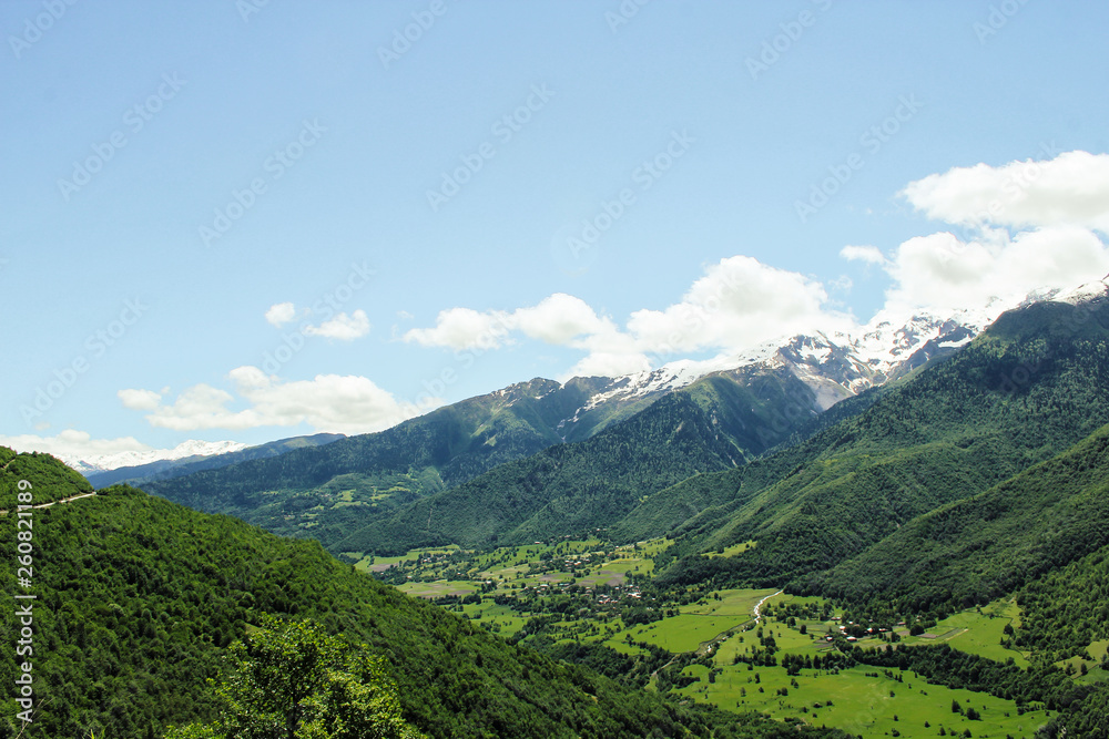 Scenic valley in the Caucasus Mountains with a small village, summer greens and snow-capped peaks