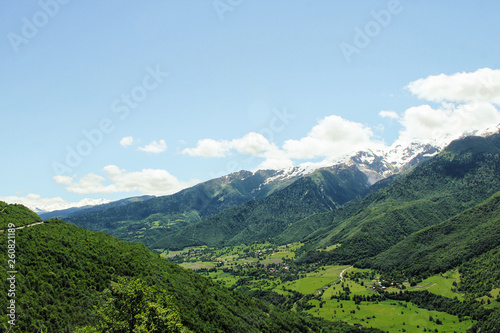 Scenic valley in the Caucasus Mountains with a small village, summer greens and snow-capped peaks