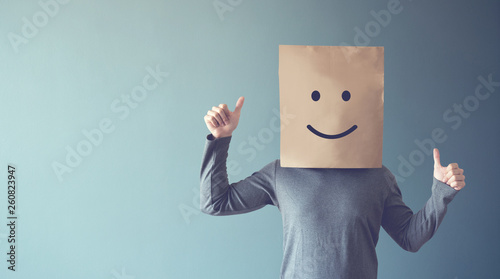 Man covering his face with a smiling face emoticon, copy space.