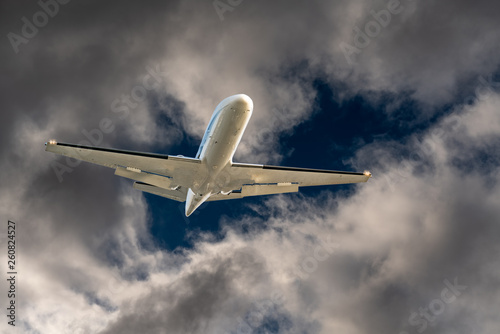 White airplane jet flying through a hole in dark dangerous and dramatic storm clouds