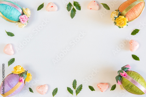 Frame of Easter eggs, leaves, and candy on sold white background