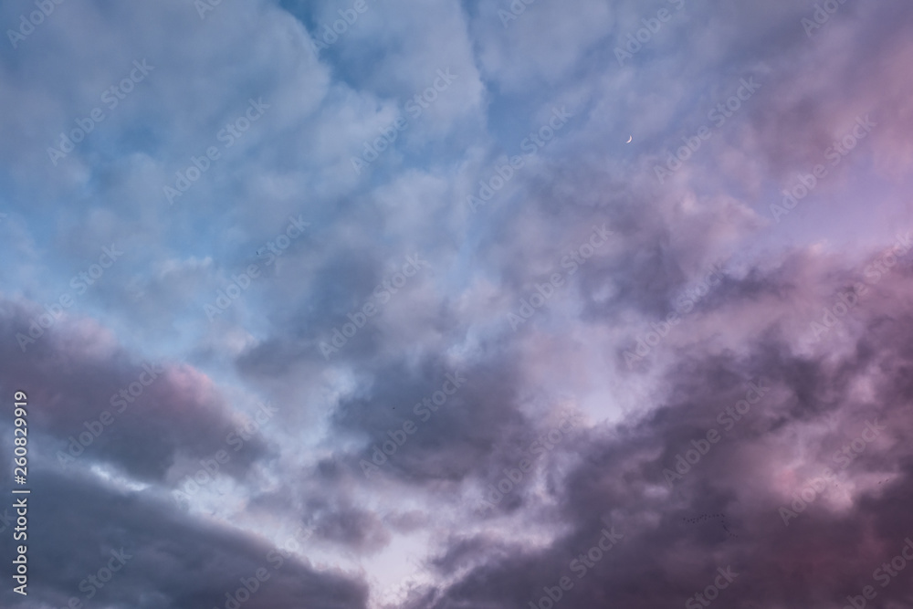 Blue sky background with evening fluffy curly rolling altocumulus altostratus clouds with setting sun. Good windy weather