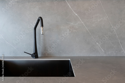 A black sink and a matt-finish black faucet set against grey surfaces made of porcelain slabs that mimic the look of natural stones