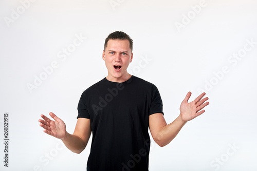 Attractive surprised man standing and looking at camera dressed in black shirt on white background.