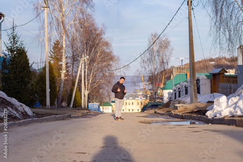 A young man in a black jacket on the street of Sespel against the Volga river in Cheboksary in early spring photo