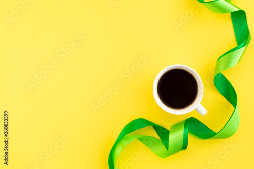 A cup of coffee with green silk ribbons on yellow background. Design minimal concept. Mocup