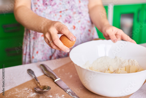 Cracking an egg to a flour. Close-up of woman's hands breaks an egg for pastry