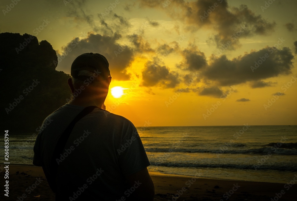 Fantastic view of silhouette of a man standing on the beach watching sunrise up from the mountain with reflection in the sea,  dramatic clouds on the background, Chumphon province Thailand.