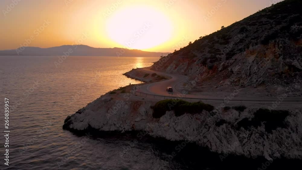 AERIAL: Car driving along the scenic road winding along the picturesque shoreline of Lefkada. Tourists on fun road trip explore the Mediterranean island at sunrise. Colorful summer sunset in Greece. AERIAL: Car driving along the scenic road winding along the picturesque shoreline of Lefkada. Tourists on fun road trip explore the Mediterranean island at sunrise. Colorful summer sunset in Greece.