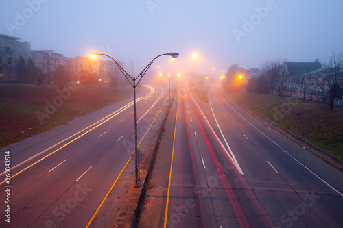 Highway at foggy night with bright trails of light from incoming and outgoing traffic.