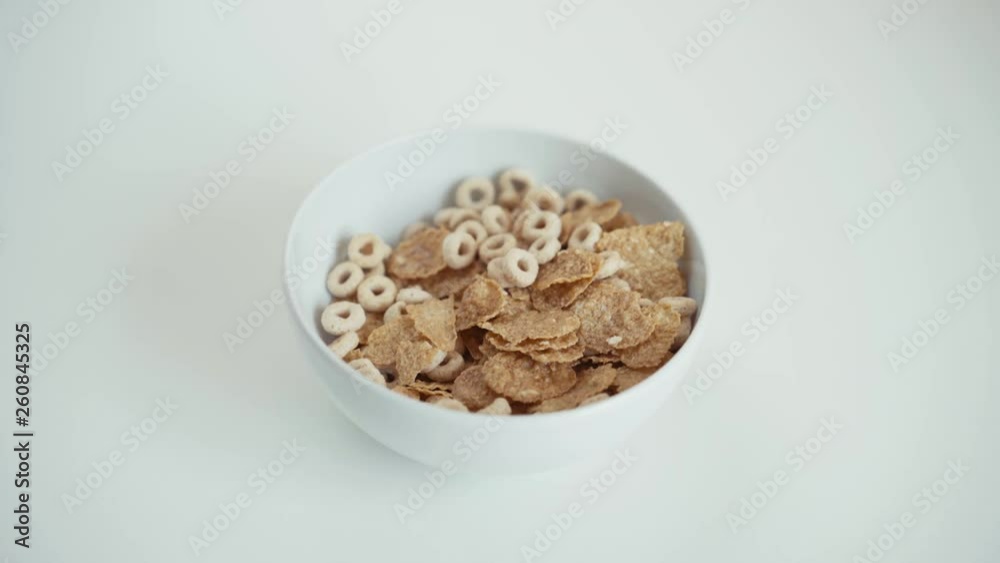 Cereals and cornflakes dropping into a white bowl in slow motion. White background Cereals and cornflakes dropping into a white bowl in slow motion. White background