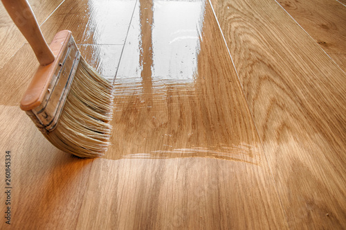 a large wooden brush covers the parquet with lacquer photo