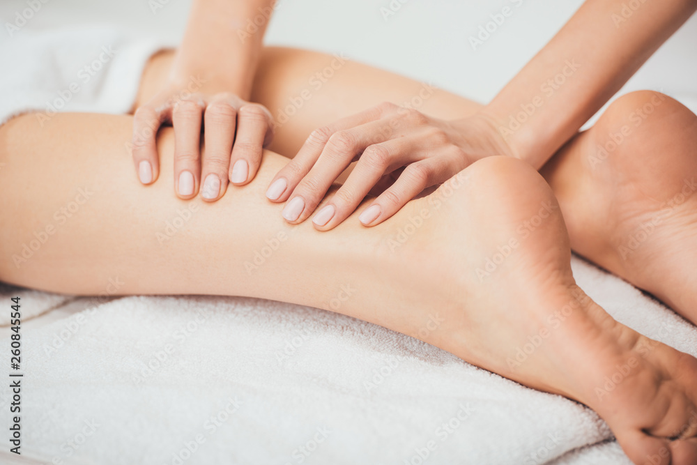 partial view of masseur doing foot massage to adult woman in spa