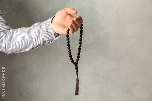Man hold prayer beads in hand against grey background