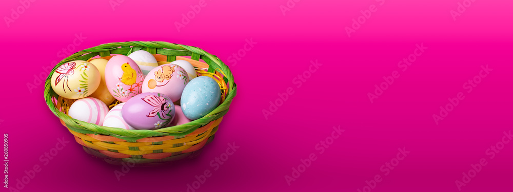 Wicker basket with Easter eggs hand painted on color tabletop background