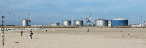 People at the large Matosinhos Beach in front of some petrol tanks in Porto harbor photo