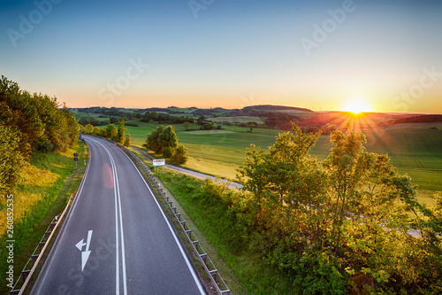 Landstraße durch idyllische grüne Landschaft zum Sonnenuntergang