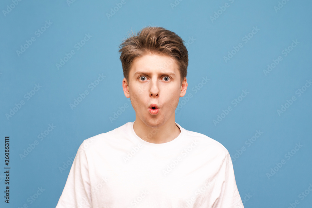 Close up portrait of an adorable guy on a blue background, look into the camera with an open mouth. Emotional young man is isolated on a blue background. Close up portrait of an adorable guy on a blue background, look into the camera with an open mouth. Emotional young man is isolated on a blue background.