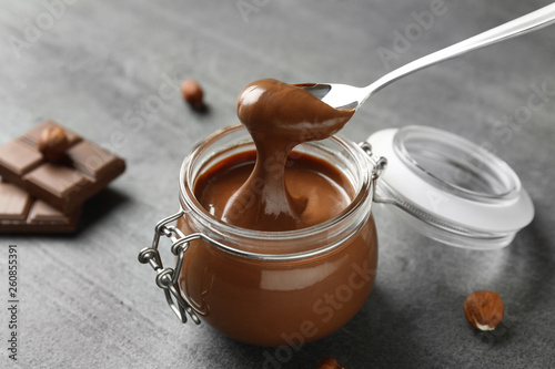 Spoon with tasty chocolate cream over full jar on table