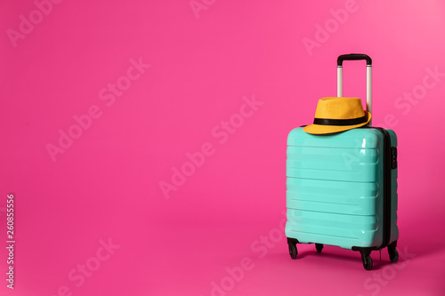 Stylish suitcase with hat on color background. Space for text