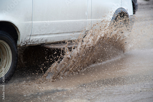 Moving car sprays puddle when heavy rain drops on concrete.