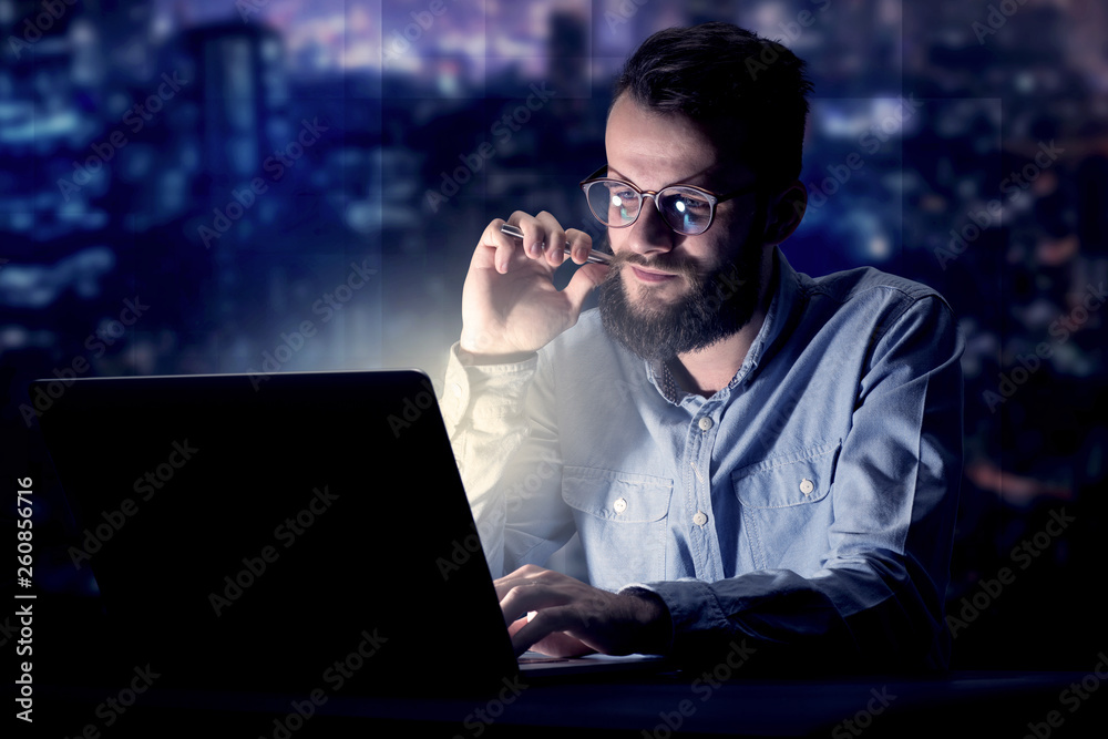 Young handsome businessman working late at night in the office with blue lights in the background Young handsome businessman working late at night in the office with blue lights in the background