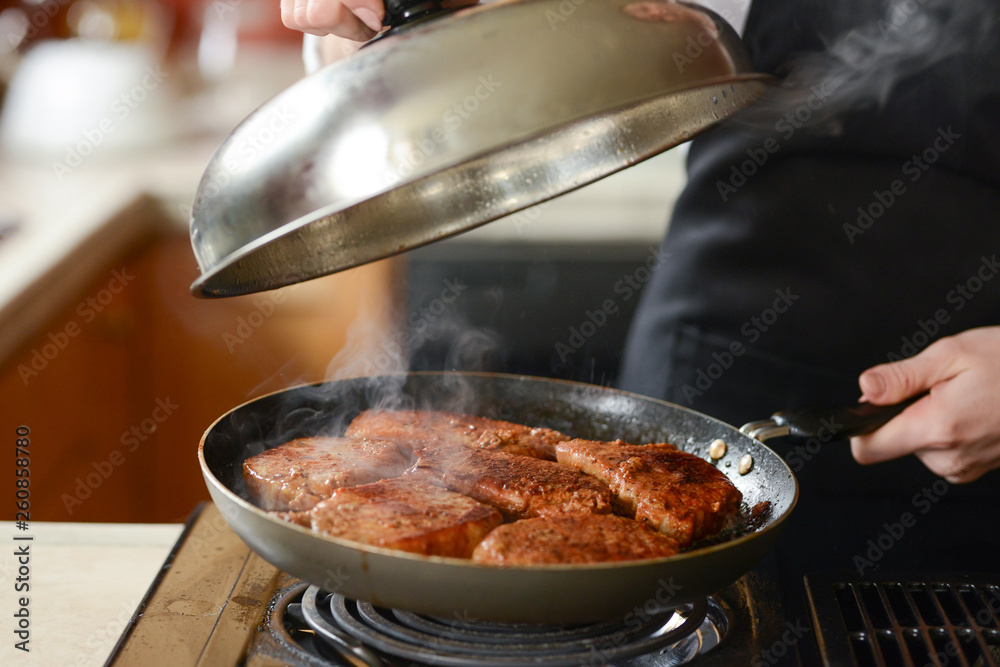 The chef in the kitchen prepares fresh pork steaks on a griddle with steam, the menu is homemade cooking culinary recipes. restaurant menu. Delicious food, recipes and cooking The chef in the kitchen prepares fresh pork steaks on a griddle with steam, the menu is homemade cooking culinary recipes. restaurant menu. Delicious food, recipes and cooking