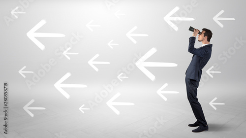 Young businessman standing and looking through binoculars with drawn arrows around
