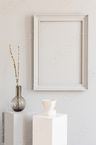 Stylish and design home decor with mock up gray poster frame, white and gray pedestals with stylish accessories ,vase with flowers. Eclectic and minimalistic room interior. Template. Blank.