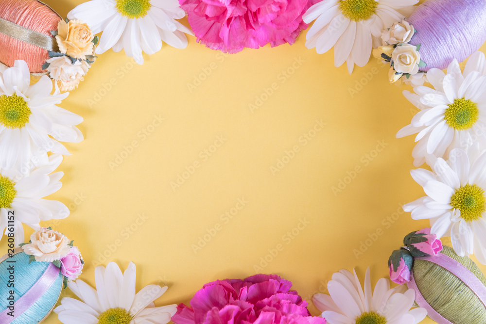 Flat lay frame of Easter eggs and flowers on solid pastel yellow background