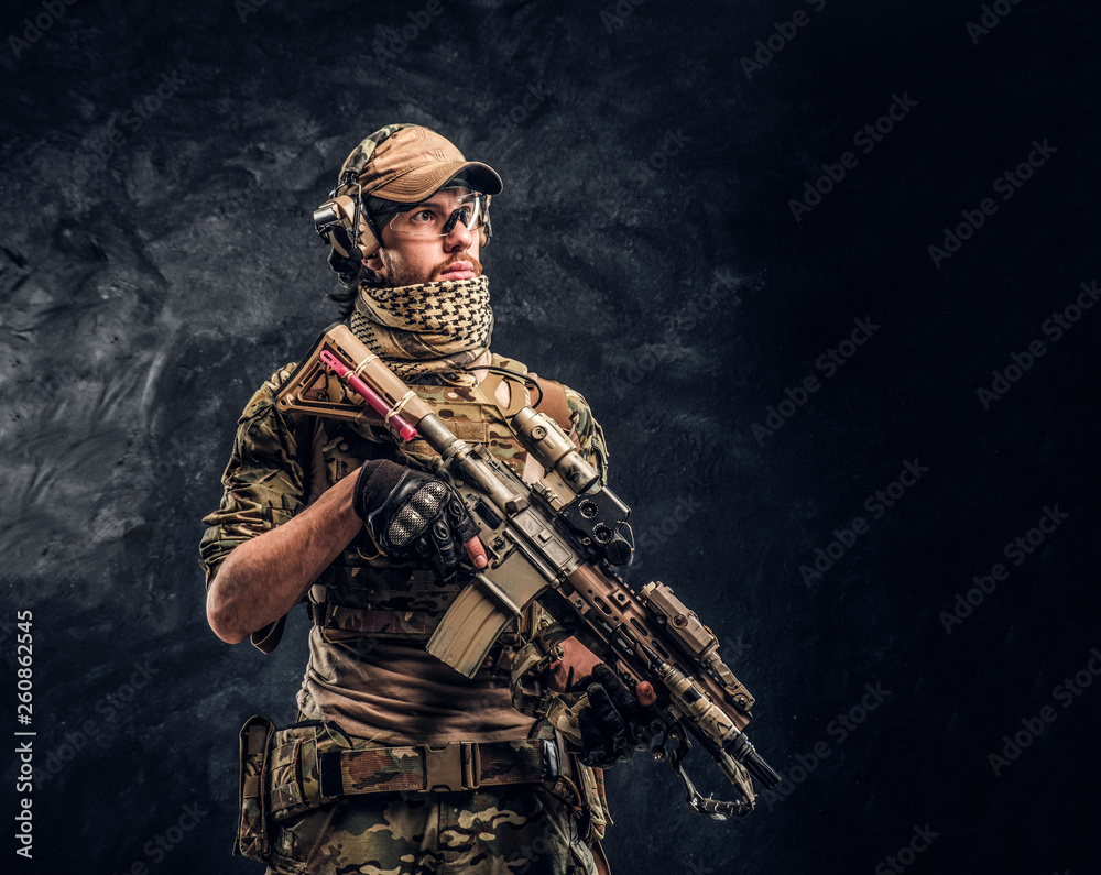 Fully equipped soldier in camouflage uniform holding an assault rifle. Studio photo against a dark wall Fully equipped soldier in camouflage uniform holding an assault rifle. Studio photo against a dark wall