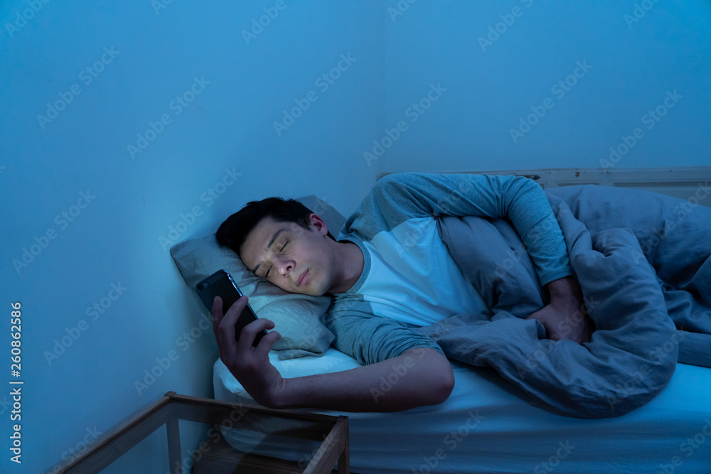 Young caucasian sleepless man bored in bed surfing on the Internet addicted to mobile phone Young caucasian sleepless man bored in bed surfing on the Internet addicted to mobile phone